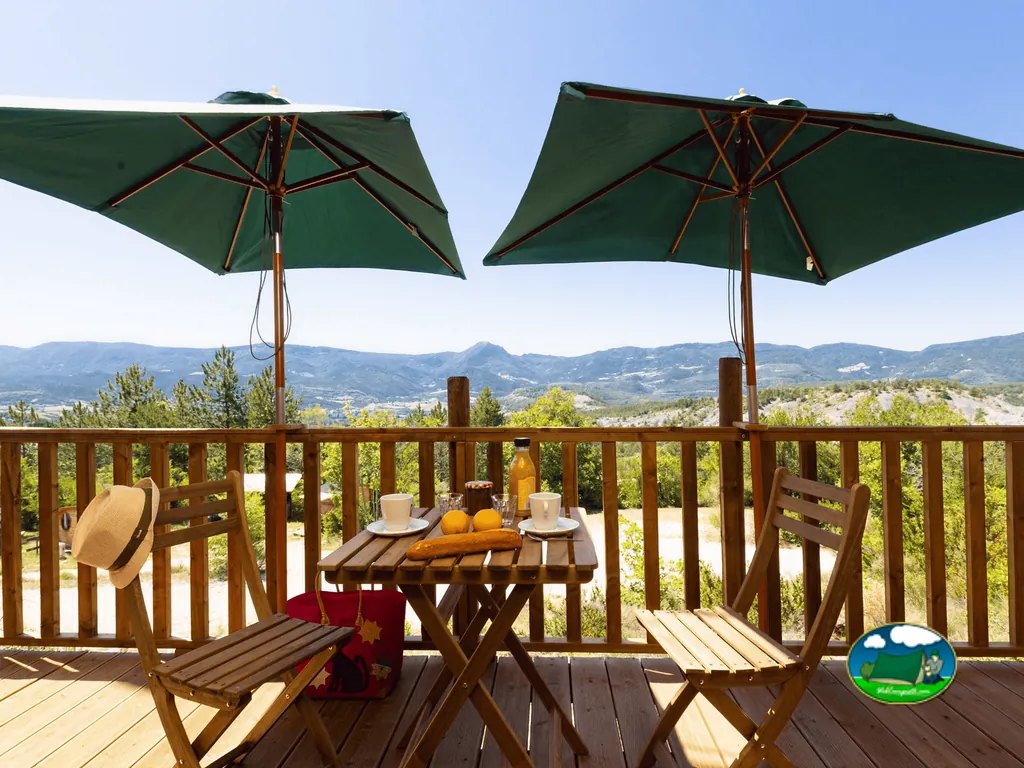 mesa de desayuno en terraza de madera con vistas a las montañas en Rosans