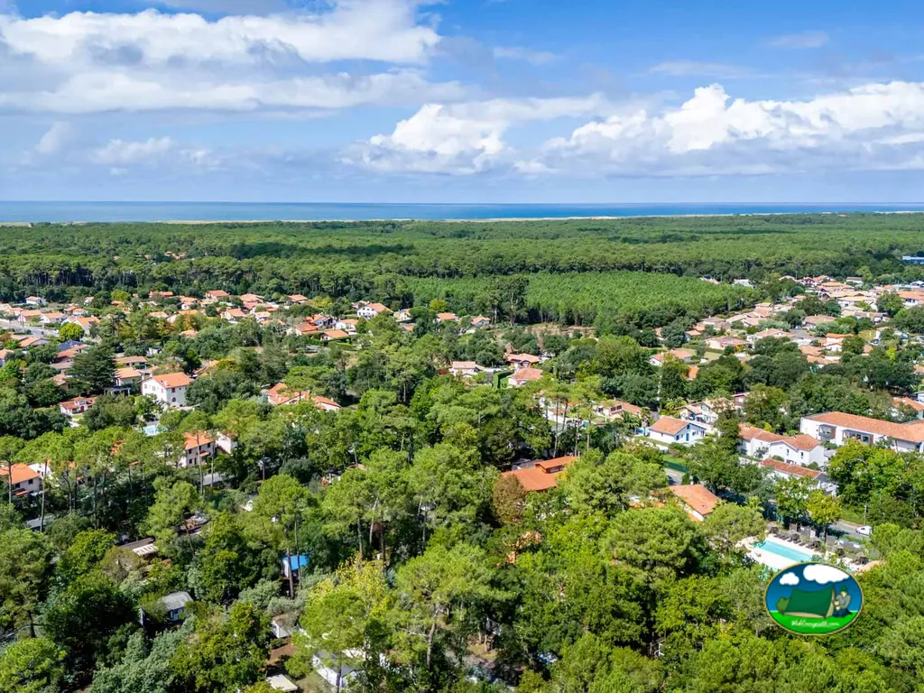vista aérea del pinar con la piscina del camping asomando entre los árboles y el mar al fondo en Ondres