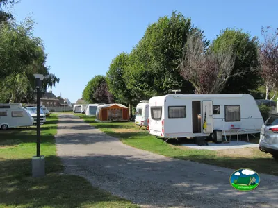 parcelas con caravanas y avances bajo grandes árboles en un camino de grava del camping en Le Crotoy