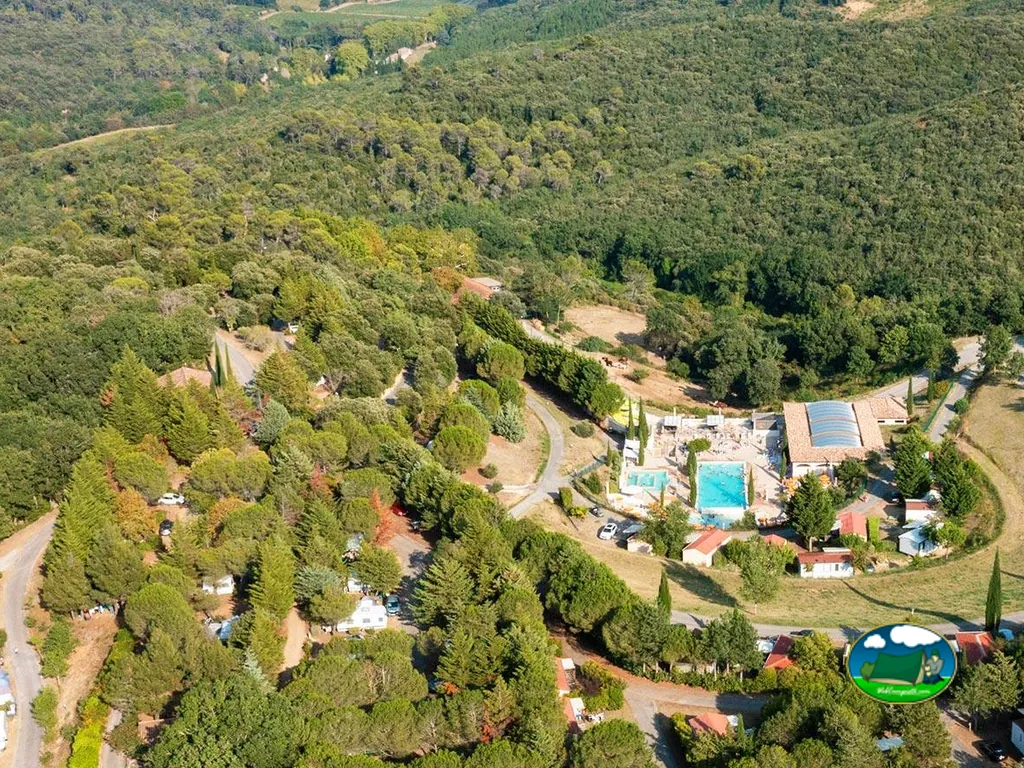 vista aérea del camping entre bosque con piscinas y bungalós en un valle arbolado