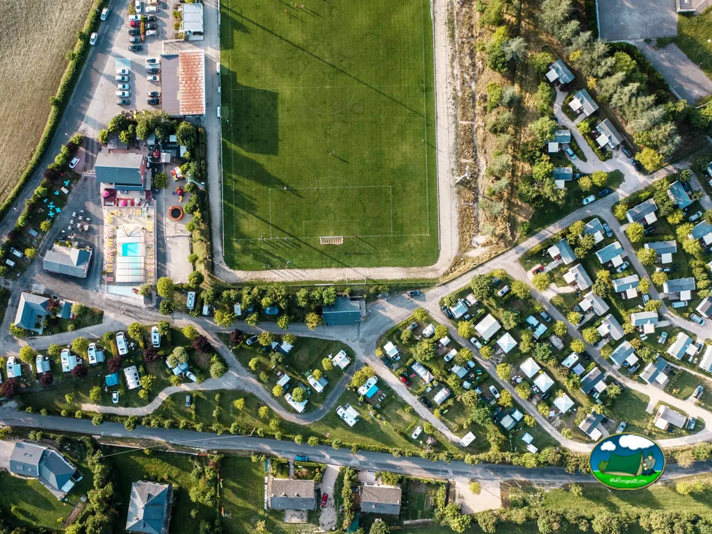 vista aérea cenital del camping junto a un campo de fútbol con piscina y parcelas arboladas
