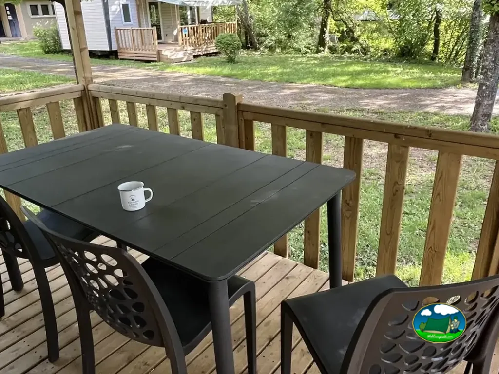 mesa y sillas en la terraza de madera de un mobil-home con vistas a otros alojamientos entre árboles