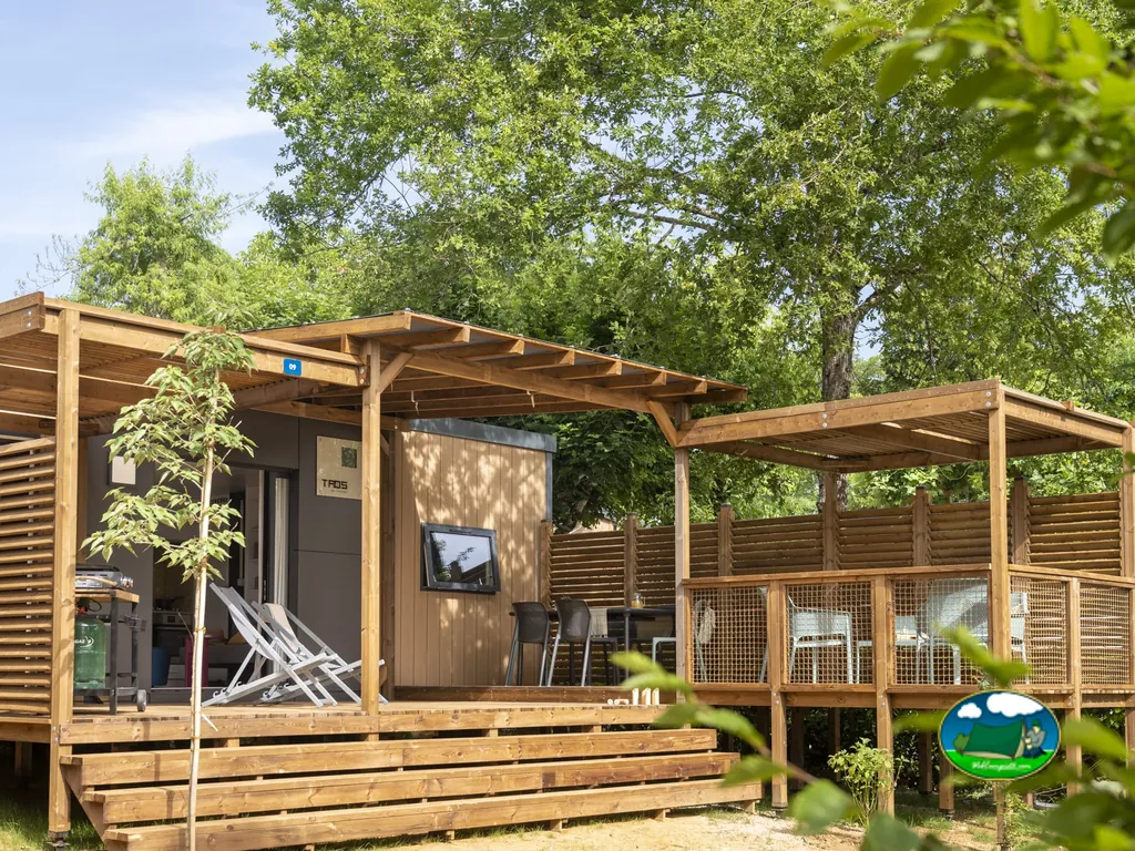 mobil-home de madera con pérgola y terraza elevada entre árboles frondosos