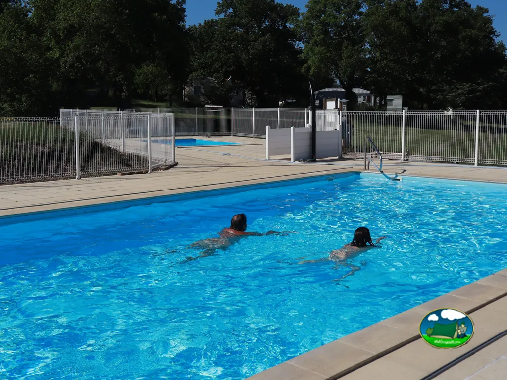 dos personas nadando de espaldas en la piscina del camping con mobil-homes al fondo