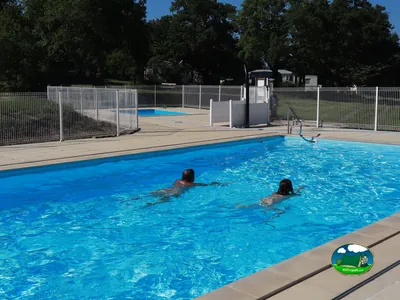 dos personas nadando de espaldas en la piscina del camping con mobil-homes al fondo