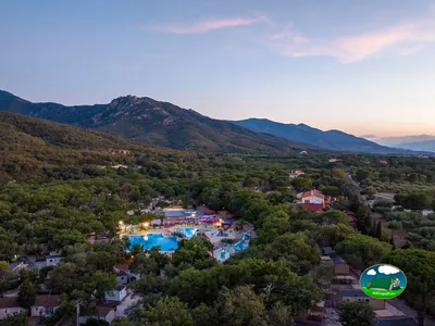 vista aérea al atardecer del camping con parque acuático iluminado entre pinares y montañas al fondo en Argelès-sur-Mer