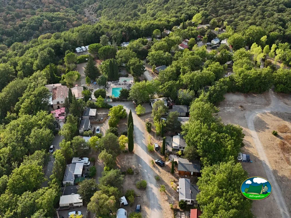 vista aérea del camping en una ladera boscosa con piscina y parcelas para caravanas entre árboles