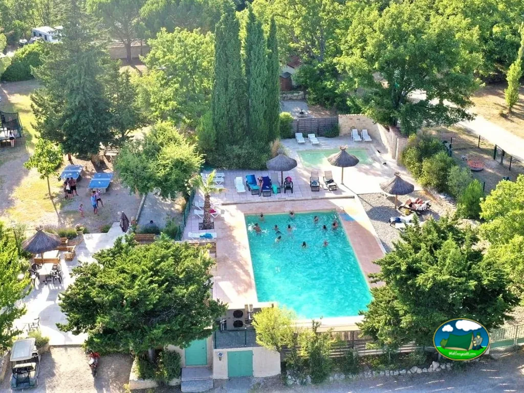 vista aérea de la piscina del camping llena de bañistas con mesa de ping-pong y hamacas alrededor entre árboles