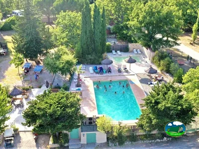 vista aérea de la piscina del camping llena de bañistas con mesa de ping-pong y hamacas alrededor entre árboles