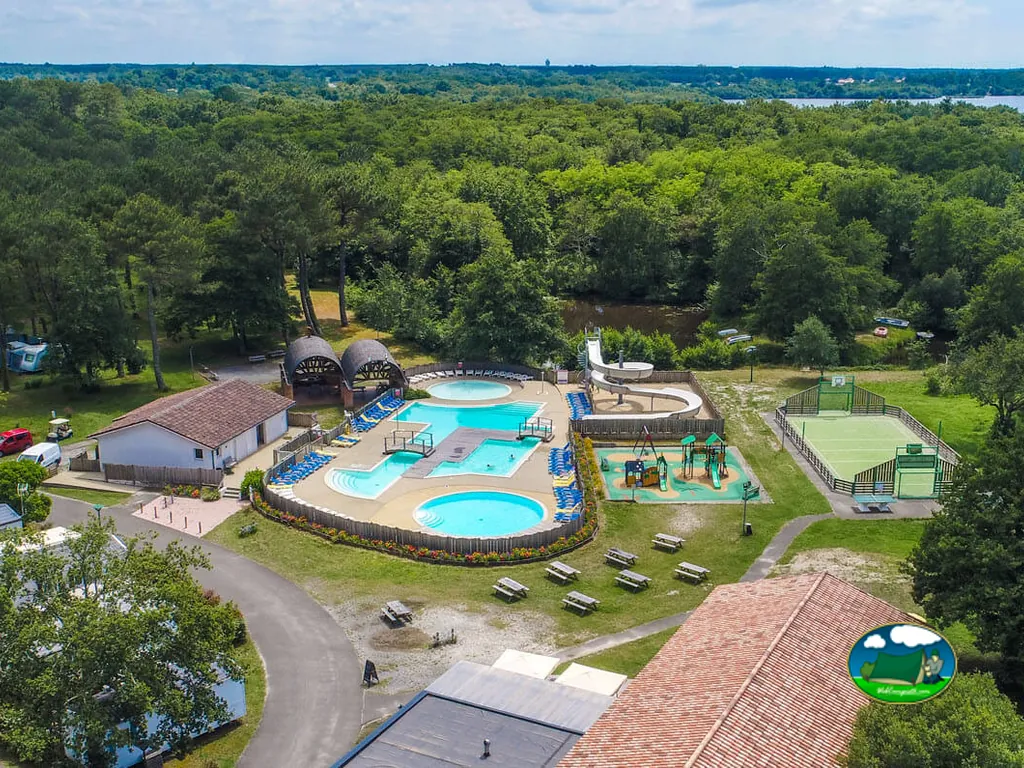 vista aérea de la piscina, parque infantil y pista deportiva del camping rodeado de bosque en Azur