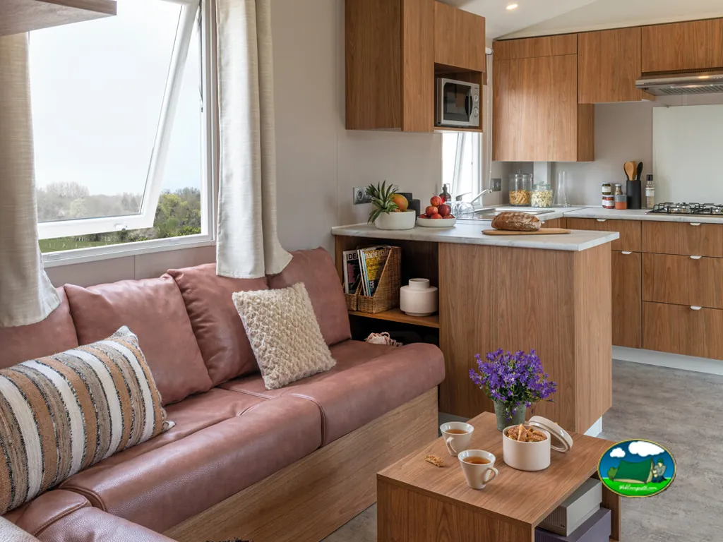 interior de mobil-home con sofá rosa, cojines y cocina abierta de madera