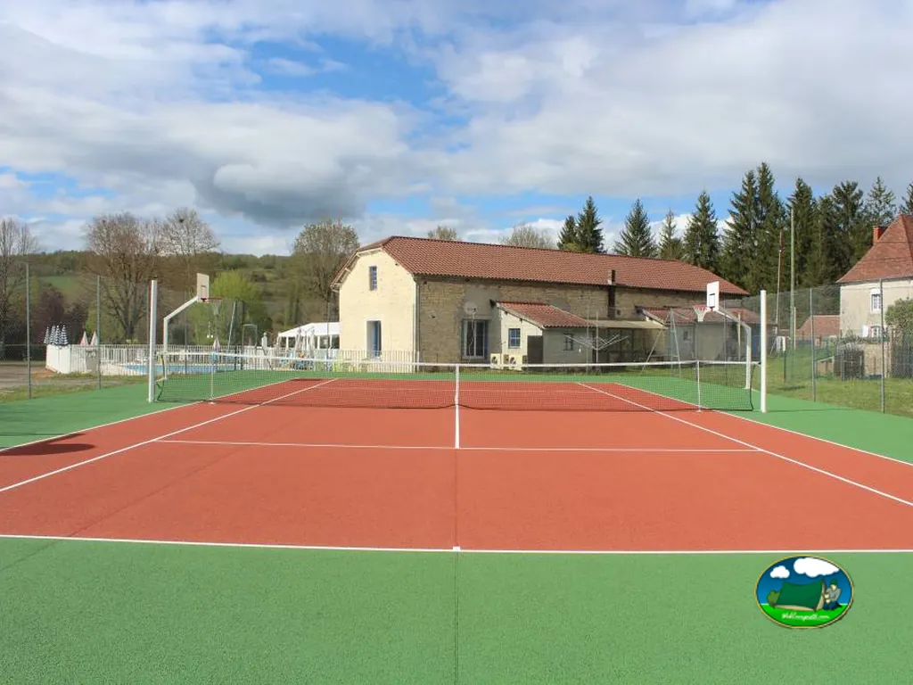 pista de tenis con piscina y edificio principal de piedra al fondo en Saint-Chamarand