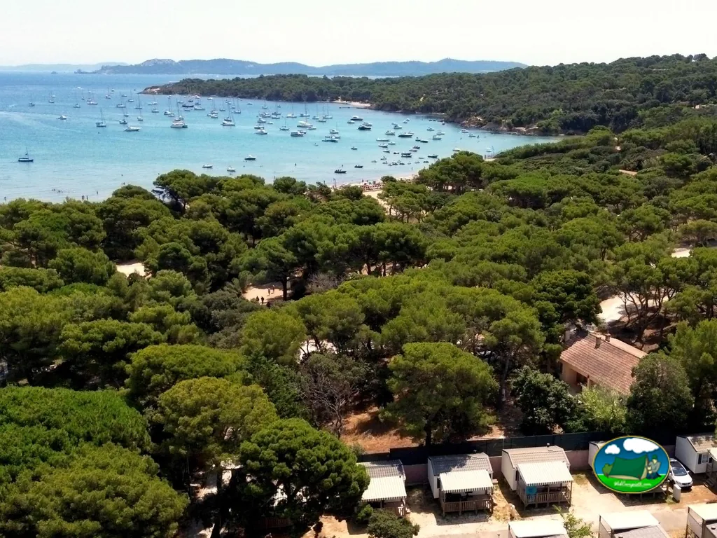 vista aérea de una bahía con veleros fondeados, pinar y bungalós del camping en Hyères