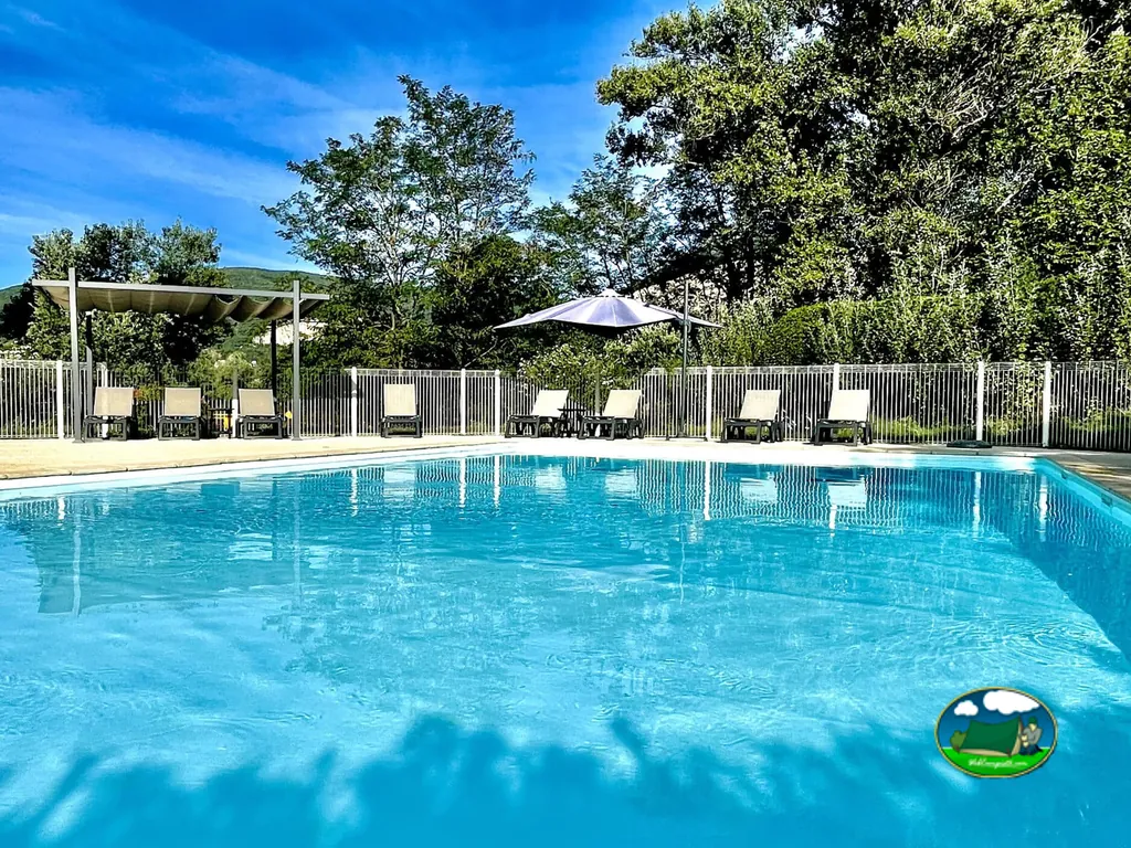 piscina azul con tumbonas, pérgola y sombrilla bajo árboles en Cruas