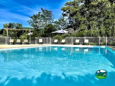piscina azul con tumbonas, pérgola y sombrilla bajo árboles en Cruas