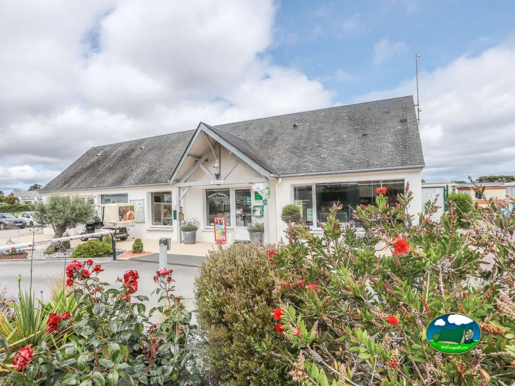 edificio de recepción del camping con tejado de pizarra y arbustos en flor en Réville