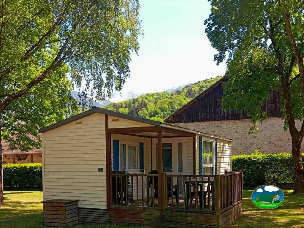 mobil-home con terraza cubierta entre árboles y montañas nevadas al fondo en Détrier
