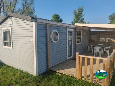 mobile home de fachada azul con porche de madera, mesa y sillas en Saint-Papoul