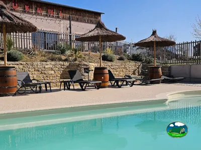 zona de piscina con sombrillas de paja sobre barricas de vino junto al restaurante en Alzonne