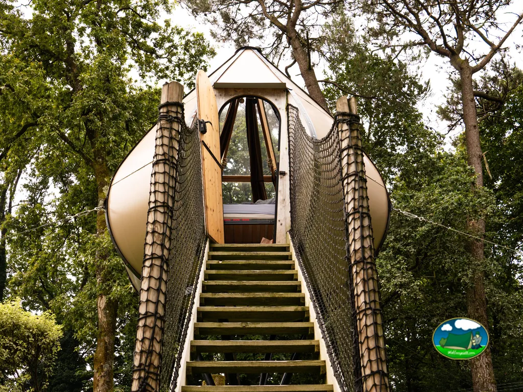 cabaña esférica elevada entre árboles, accesible por una escalera de madera y red, en el camping de Pont-Scorff