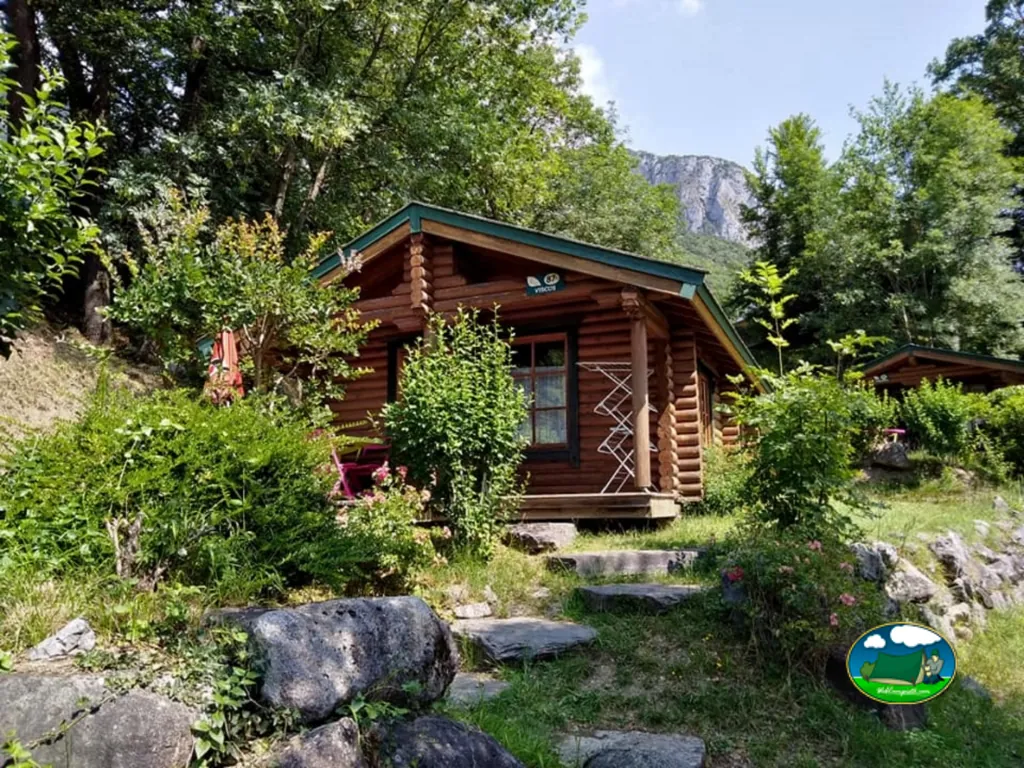 chalet de madera tipo cabaña de troncos con montañas al fondo en el camping de Agos-Vidalos