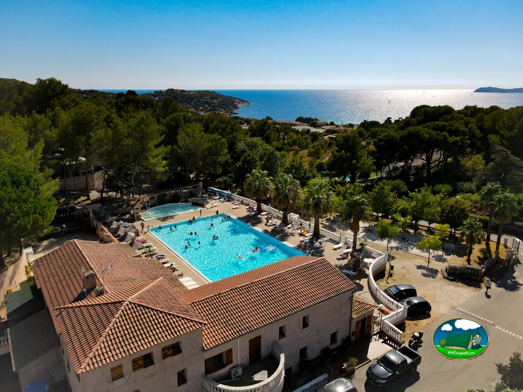 vista aérea de la piscina junto al edificio principal con el mar al fondo en el camping de Le Pradet