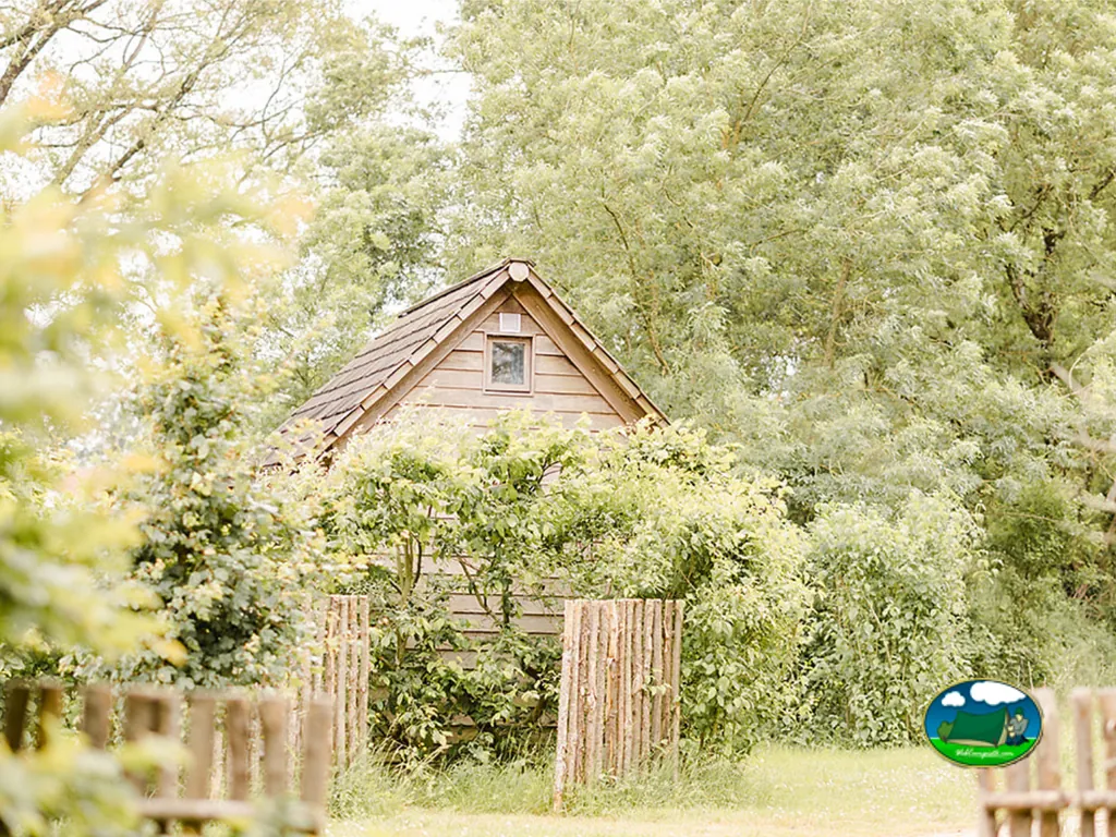 cabaña de madera cubierta de vegetación tras una valla rústica de troncos en el camping de Chauché