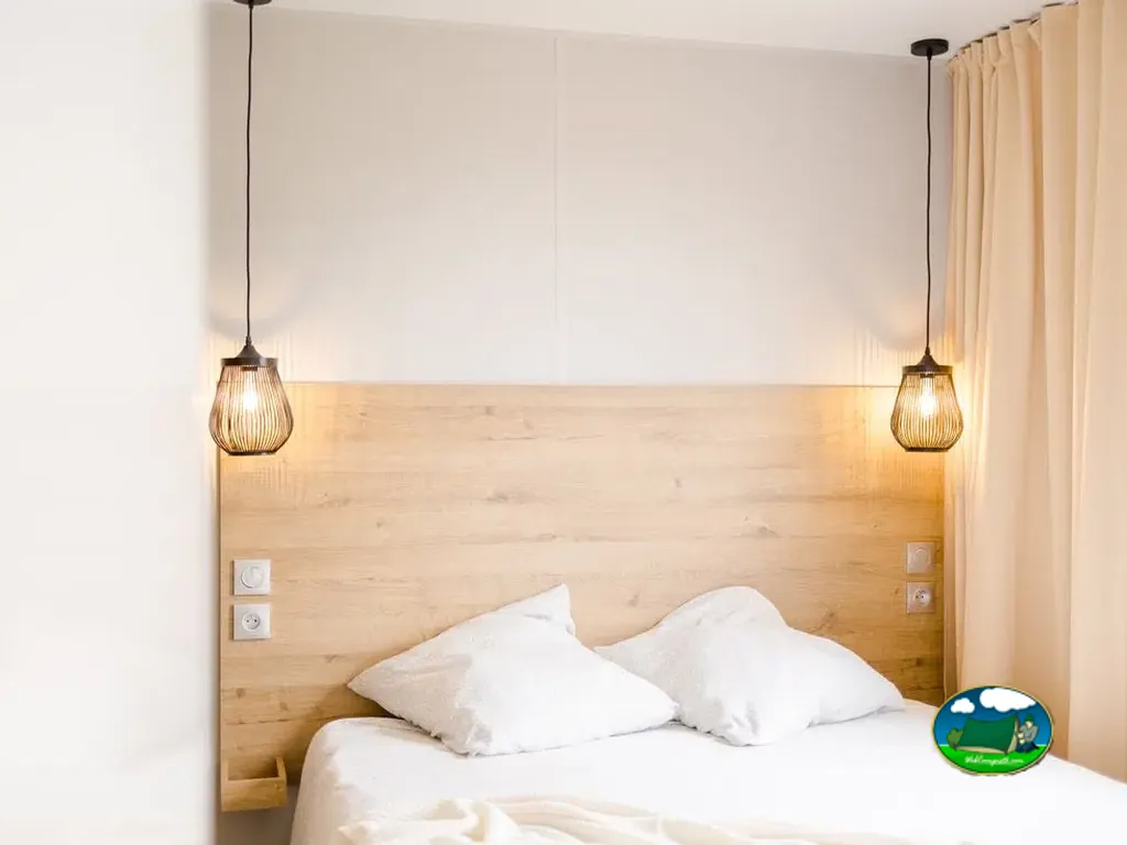 dormitorio de mobil-home con cabeceros de madera clara y lámparas colgantes en Chauché