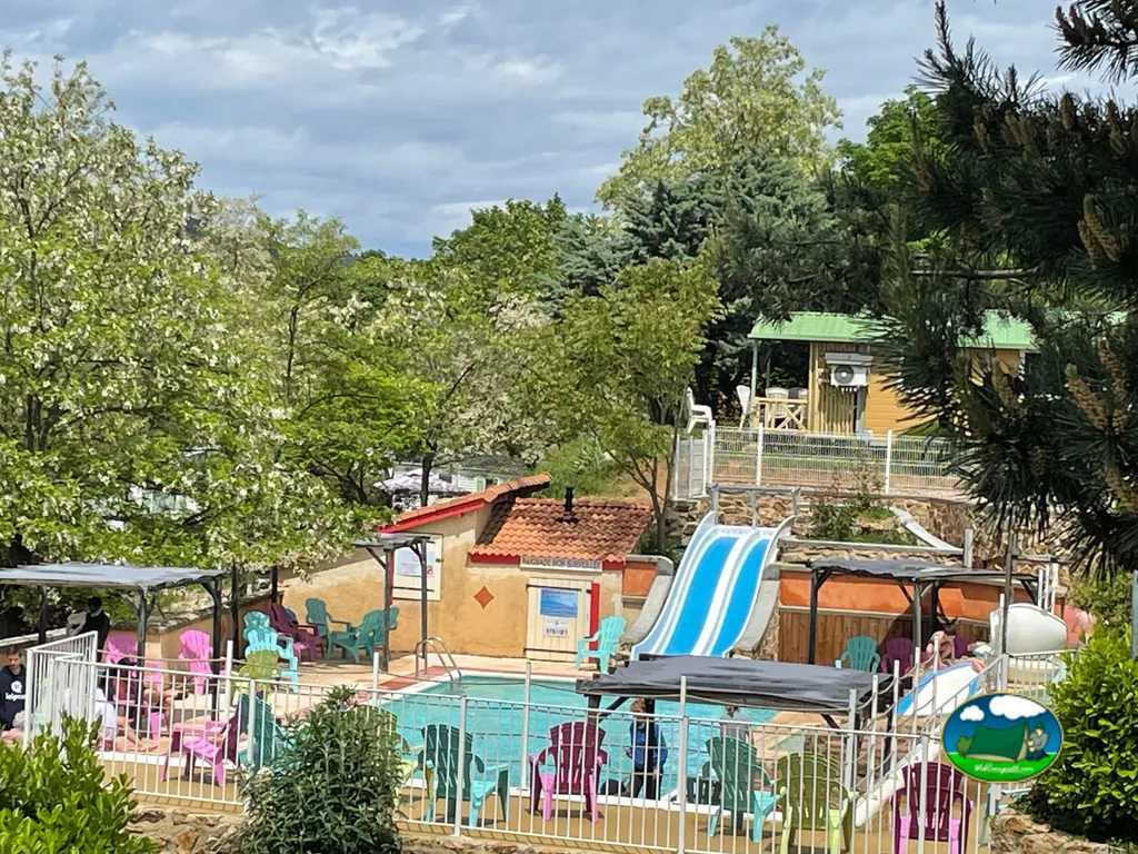 piscina con tobogán azul entre árboles y caseta de recepción del camping en Le Crestet