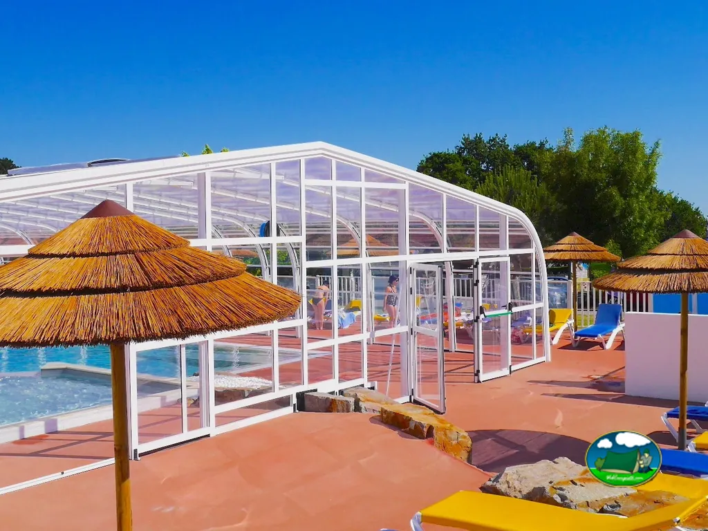 piscina cubierta acristalada con sombrillas de paja en la terraza del camping en Les Moutiers-en-Retz
