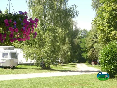 camino arbolado con caravana estacionada y flores colgantes en las parcelas del camping en Sciez