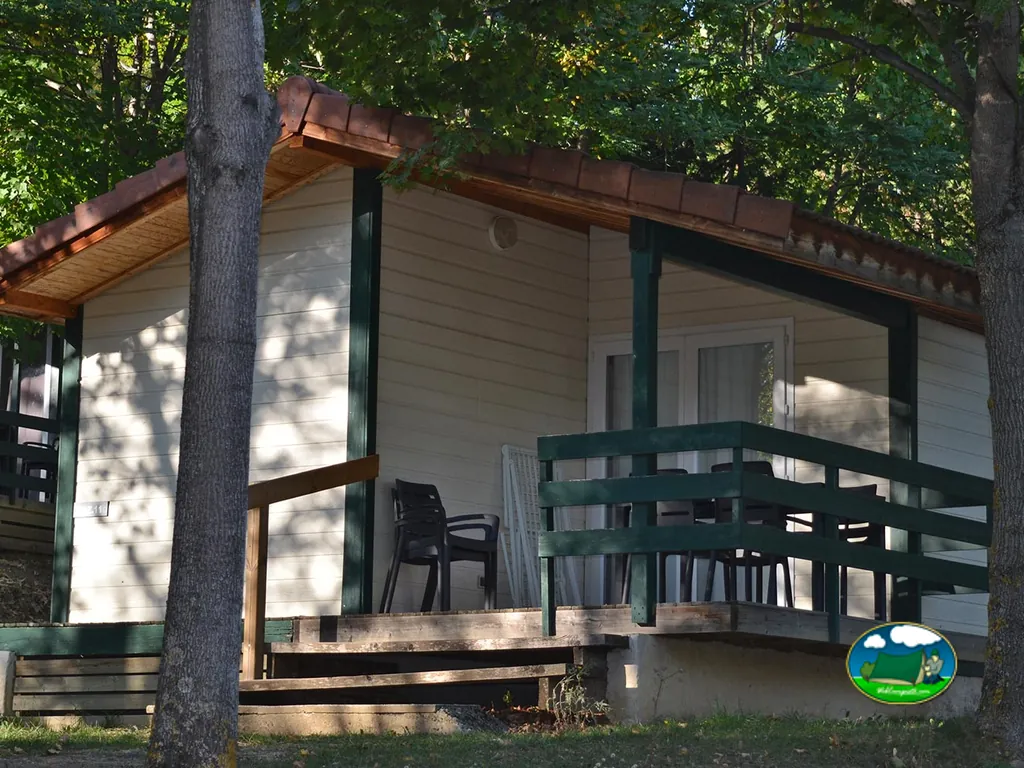 chalet de madera con terraza cubierta y mesa entre árboles en el camping de Gap