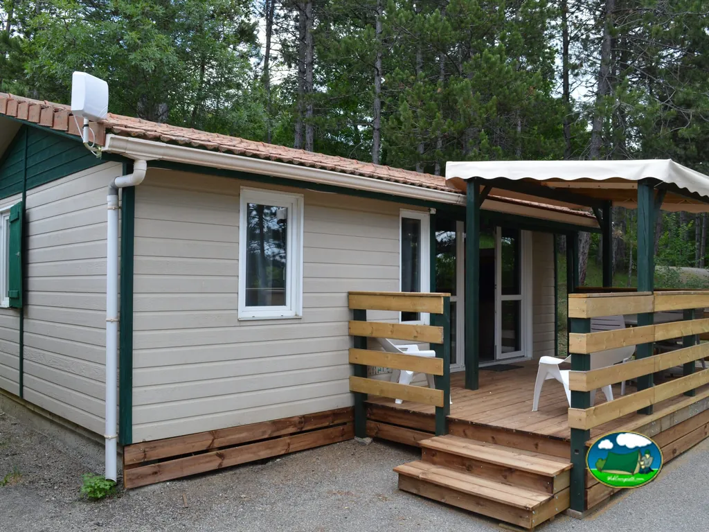 mobil-home con porche cubierto y terraza de madera entre pinos en el camping de Gap
