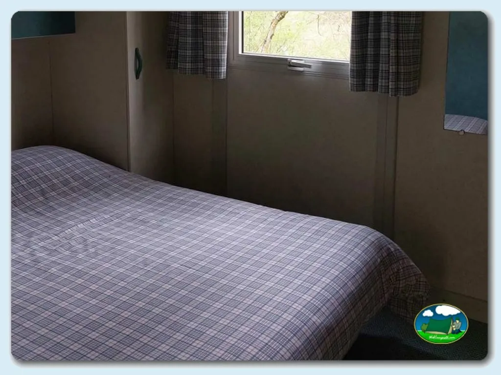 Mobil-home dormitorio con cama y ventana del Camping La Isla-Picos de Europa, Turieno (Cantabria)