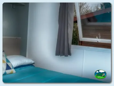 Interior mobil-home con cama y ventana del Camping Somo Parque, Ribamontán al Mar (Cantabria)