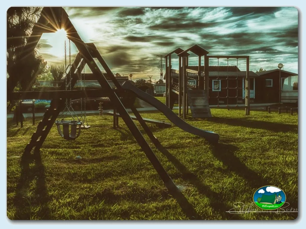 Parque infantil con tobogán y columpios, cabaña al fondo del Camping Somo Parque, Ribamontán al Mar (Cantabria)