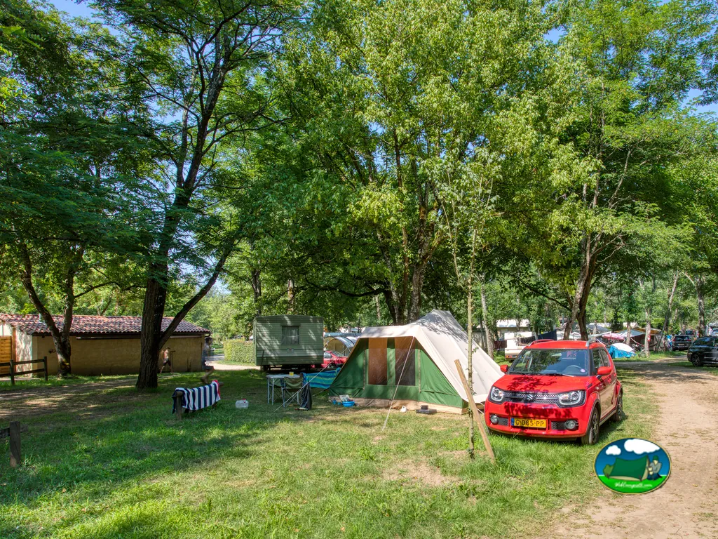 parcela sombreada con tienda de campaña, caravana y coche junto a la casa del camping en Carsac-Aillac