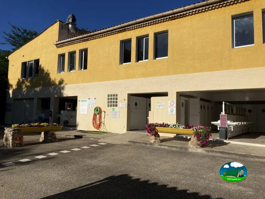 bloque de aseos con manguera enrollada y jardineras de flores