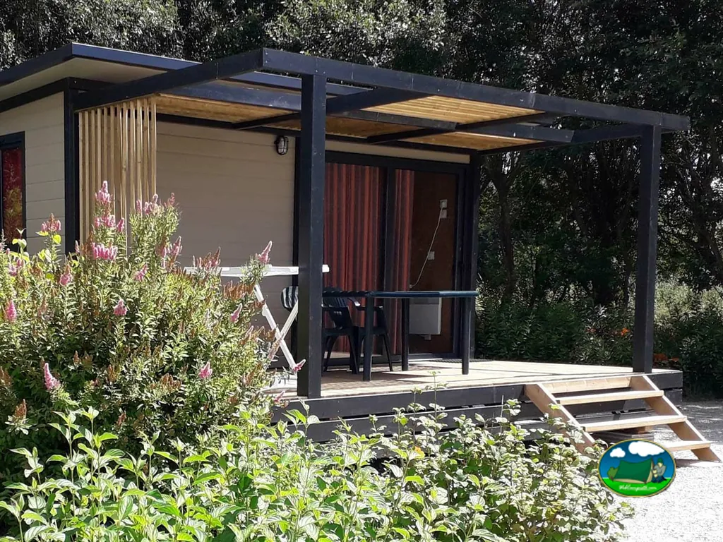 terraza cubierta con pérgola de madera y sillas junto a un bungaló del camping