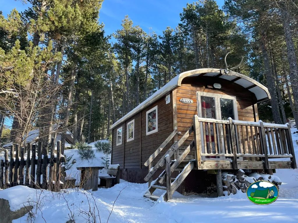 cabaña de madera tipo roulotte cubierta de nieve con escalera de acceso entre pinos