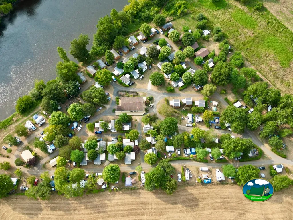 vista aérea del camping arbolado junto al río con parcelas, caravanas y coches en Carsac-Aillac