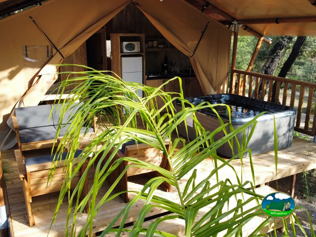 interior de una tienda glamping con cocina, jacuzzi en la terraza y bosque alrededor en Grimaud