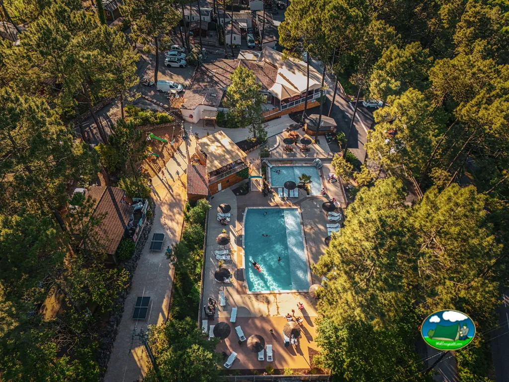 vista aérea de la piscina del camping entre pinos con bañistas en Joyeuse