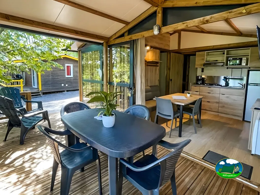 terraza cubierta con mesa y sillas junto a la cocina abierta de un mobil-home en Joyeuse