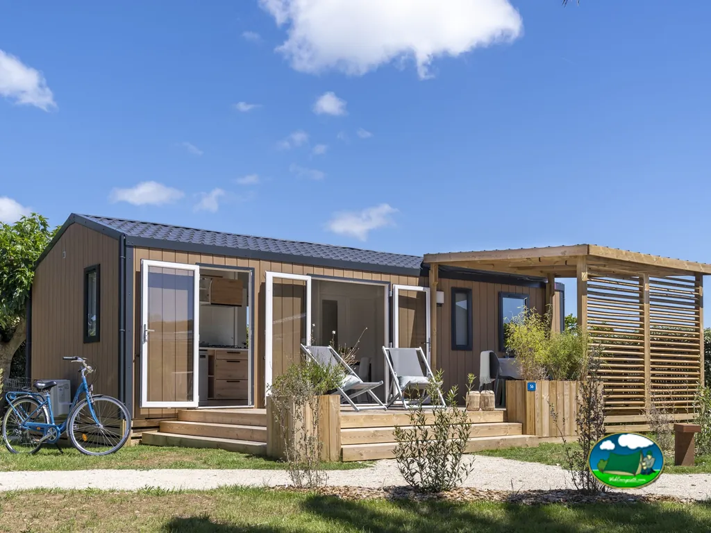mobil-home de madera con terraza, pérgola y bicicleta aparcada bajo un cielo azul en Ars-en-Ré
