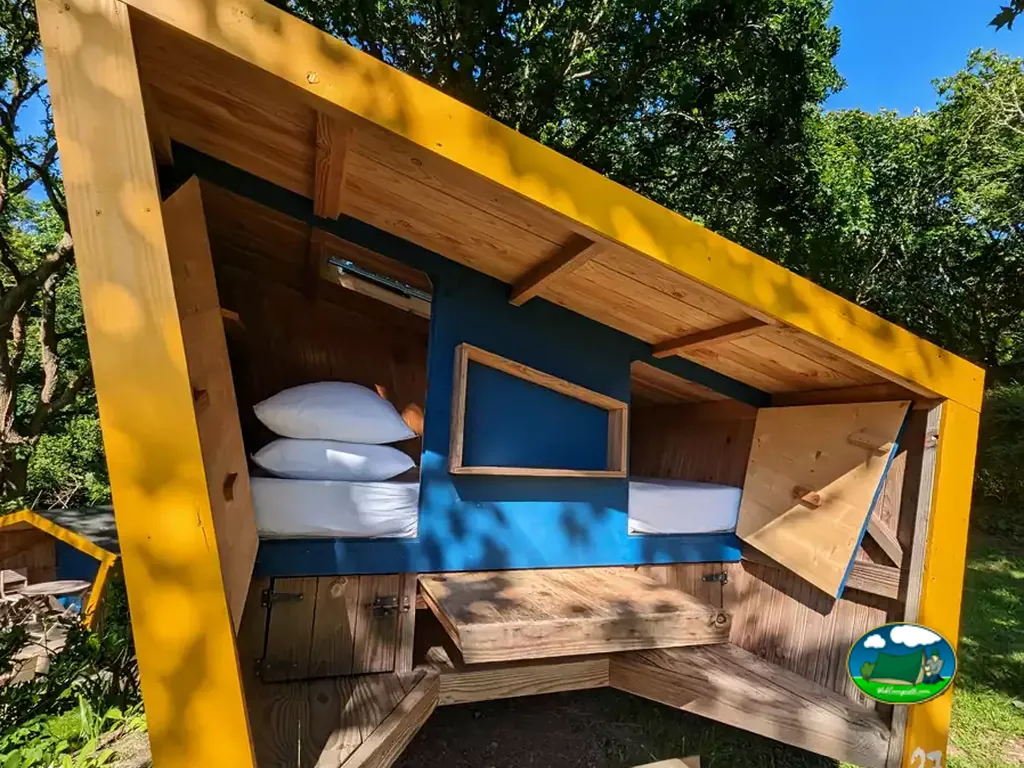 cabaña rústica con literas de madera y cojines azules bajo los árboles en Plouhinec