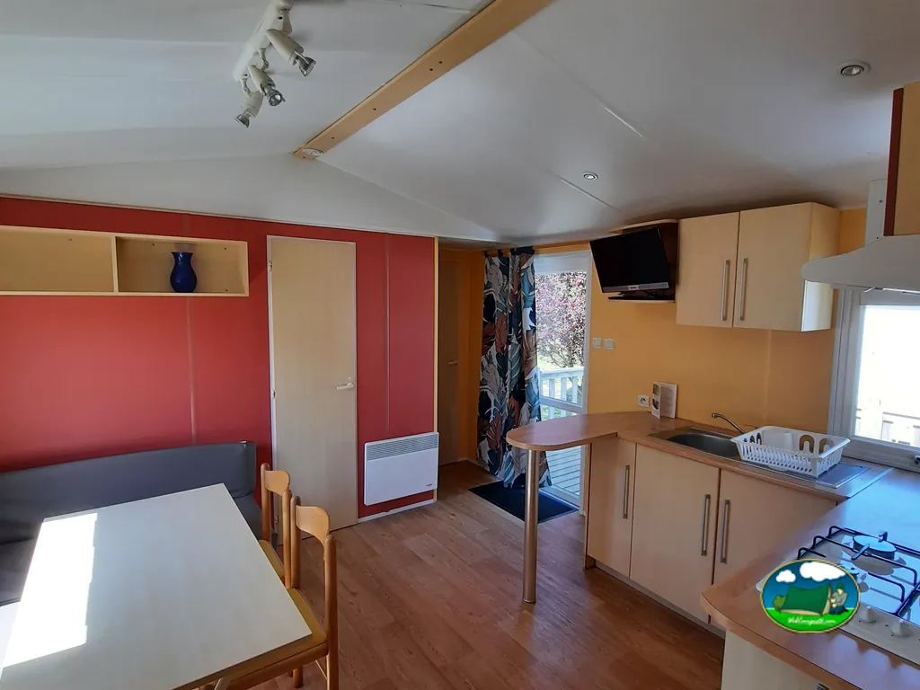 salón cocina de un mobil-home con pared roja, sofá y cocina equipada en Plouezoc'h