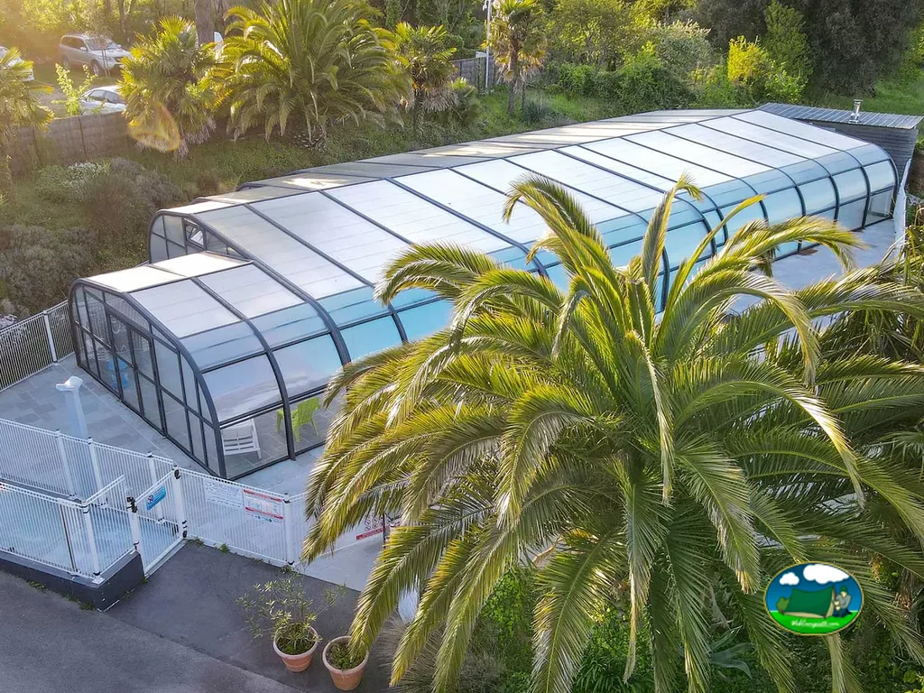 vista aérea de la piscina cubierta con techo retráctil de cristal rodeada de palmeras en Carnac