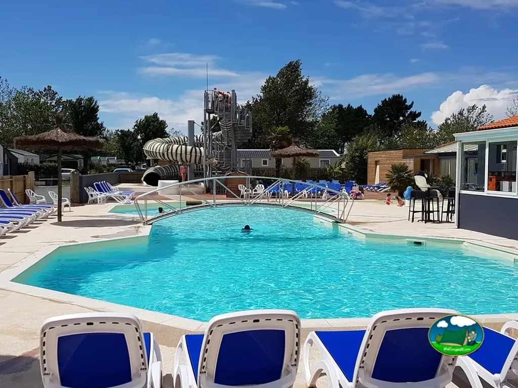 piscina con tobogán de tubo y bañistas bajo cielo despejado con mobil-homes al fondo en Saint-Vincent-sur-Jard