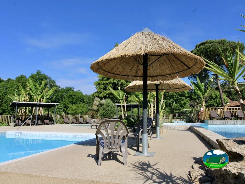 sombrilla de paja junto a piscina con tumbonas y vegetación tropical en el camping